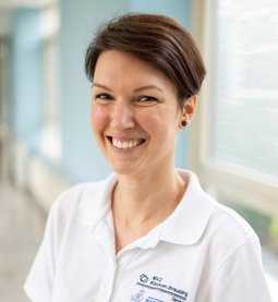 Andrea Duris (© Johannes Lehner) Portrait einer jungen Dame mit braunem Kurzhaarschnitt, freundlich lachend und weißem Poloshirt mit Logo