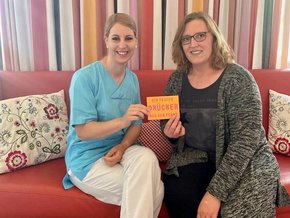 Postkartenaktion (© Stephanie Seckel) Das Foto zeigt die onkologische Fachkrankenschwester Michaela Winhart (rechts) und die Stationsleiterin Julia Rinkl, die bei onkologischen Pflegevisiten die mutmachenden Postkarten an Krebspatientinnen verteilen.