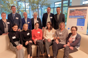 Gefäßtag 2025 (© Ursula Eisenmann) Die vordere Reihe sitzt am runden Sofa des Foyers, die hintere stehend. Daneben ein Rollup.