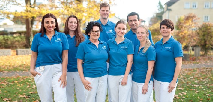Team MVZ Pneumologie (© Johannes Lehner) Acht Personen in weißen Hosen und dunkelblauen Poloshirts im herbstlichen Patientengarten als Gruppe posierend
