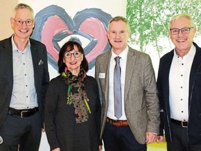 Herztag 2025 (© Theodor Huber) Vor dem RollUp der Herzstiftung die Herren mit Jackett, rechts mit Jacke, Frau Mehr am kleinsten mit schwarzem Pulli und buntem Schal. Alle Brille und lachend.