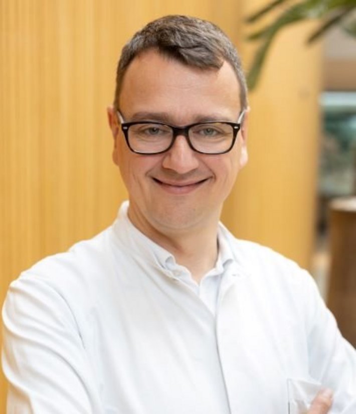 Dr. Daniel Vagedes (© Johannes Lehner) Portrait von lächelndem Arzt mit braunen Haaren und schwarzer Brille
